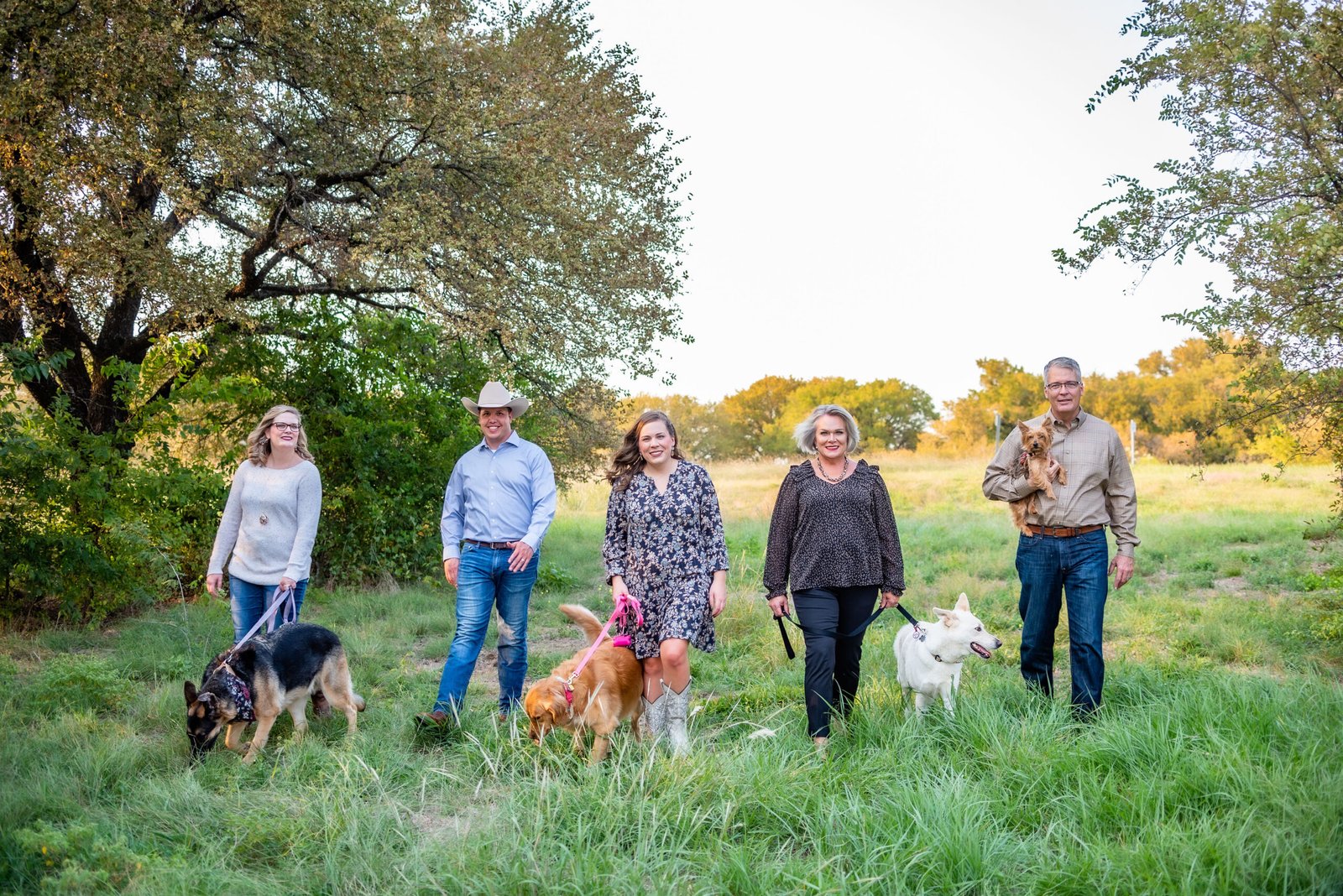 Family walking with their dogs in a scenic green field during golden hour at Canyon Falls, Flower Mound, Texas, in the fall season, highlighting a warm and natural outdoor portrait photography setting